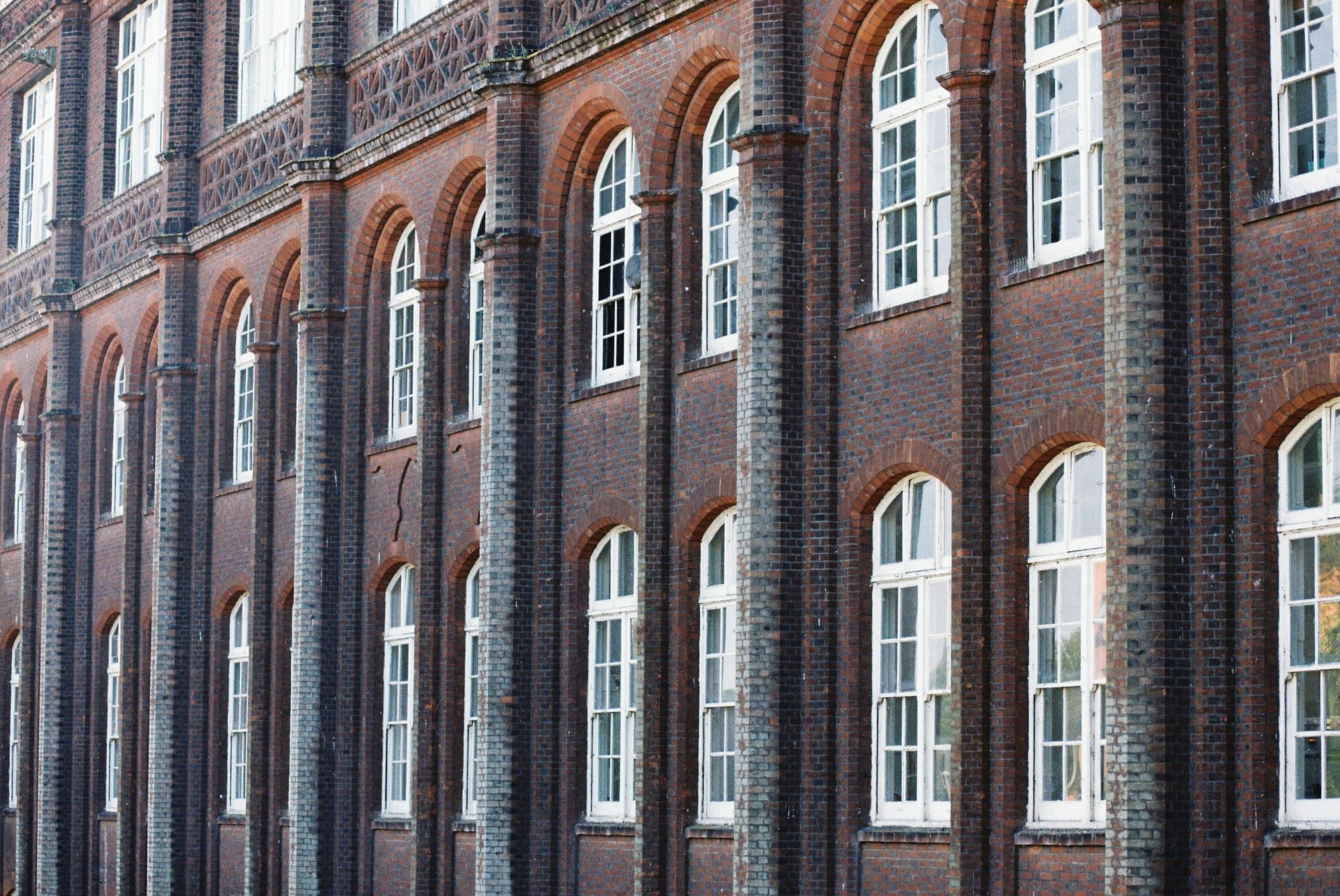 Facade of an older dark brick building with brick pilasters and rows of tall arched windows with white sash