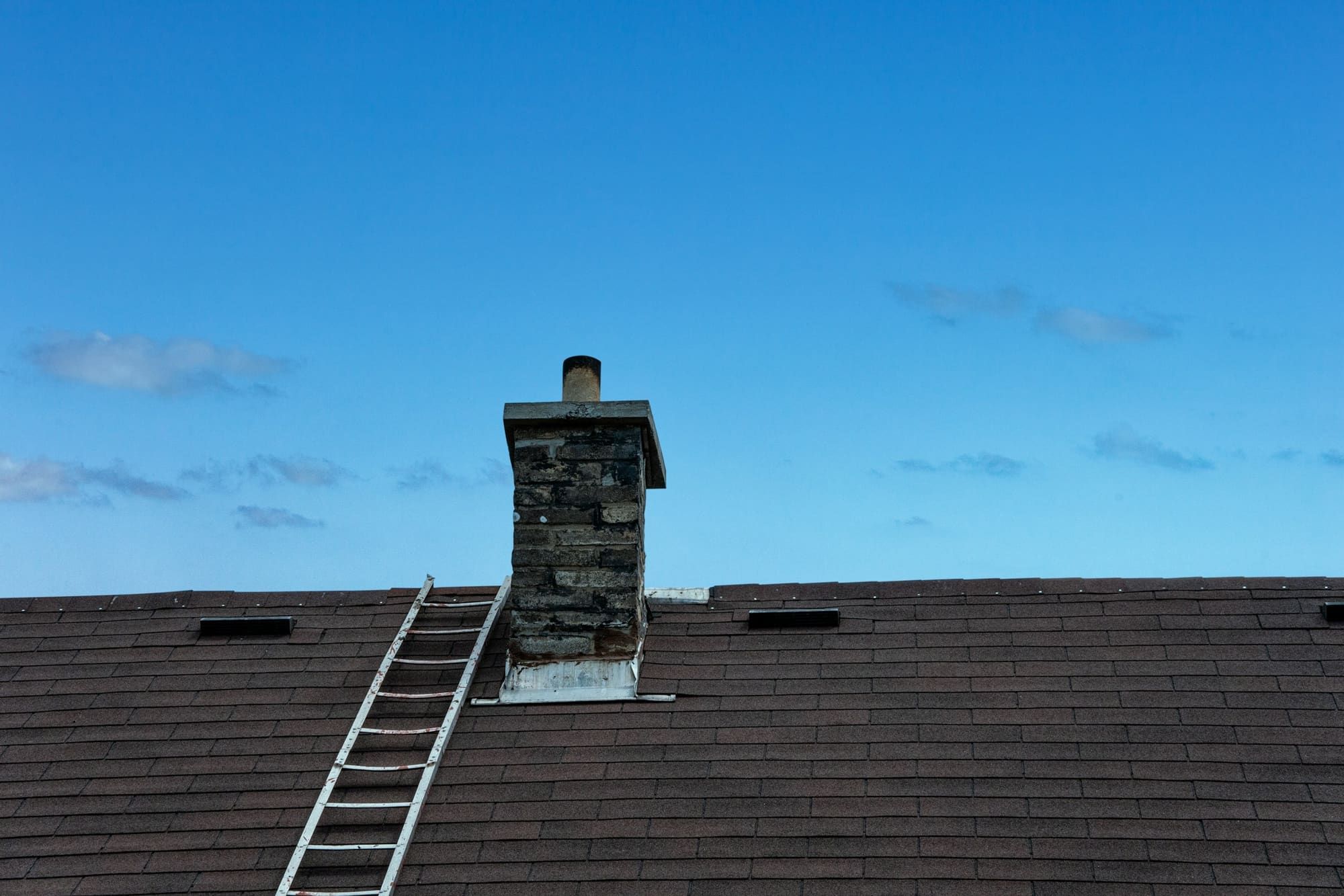Roof ladder laid up a dark shingle roof to a masonry chimney with metal flashing at its base