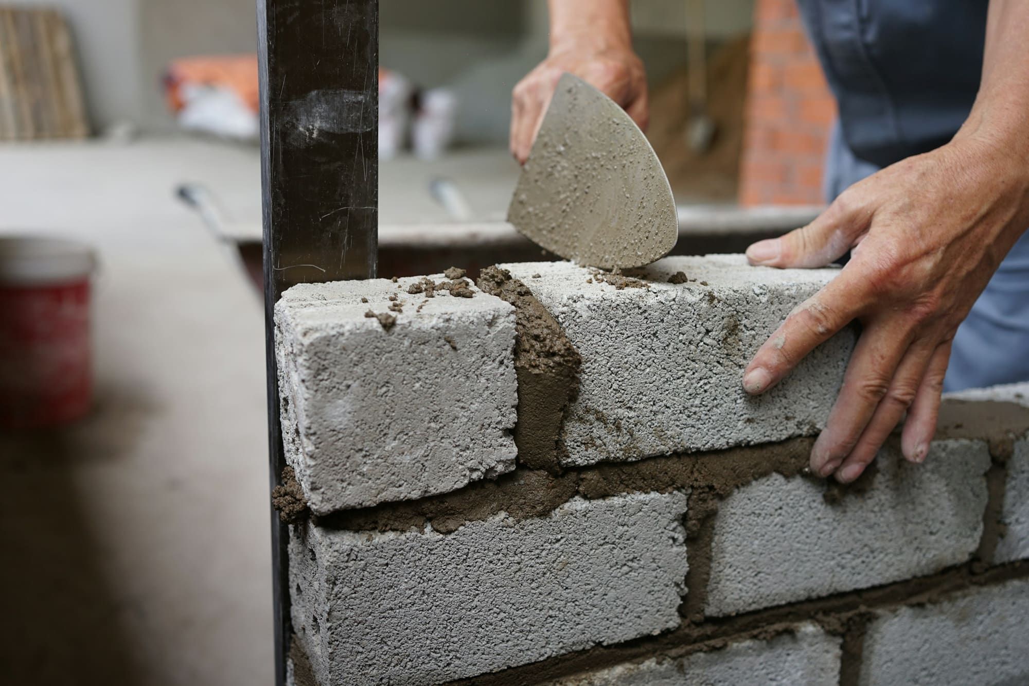 One hand pressing a concrete block into wet mortar on a block wall while the other holds a mortar-covered trowel